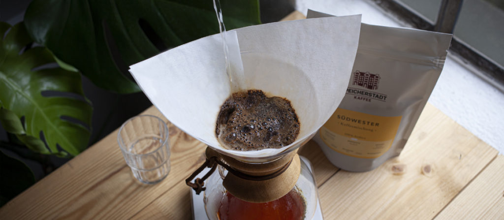 Ein Kaffee wird in einer Chemex zubereitet. Daneben steht eine Packung Südwester Kaffeemischung.